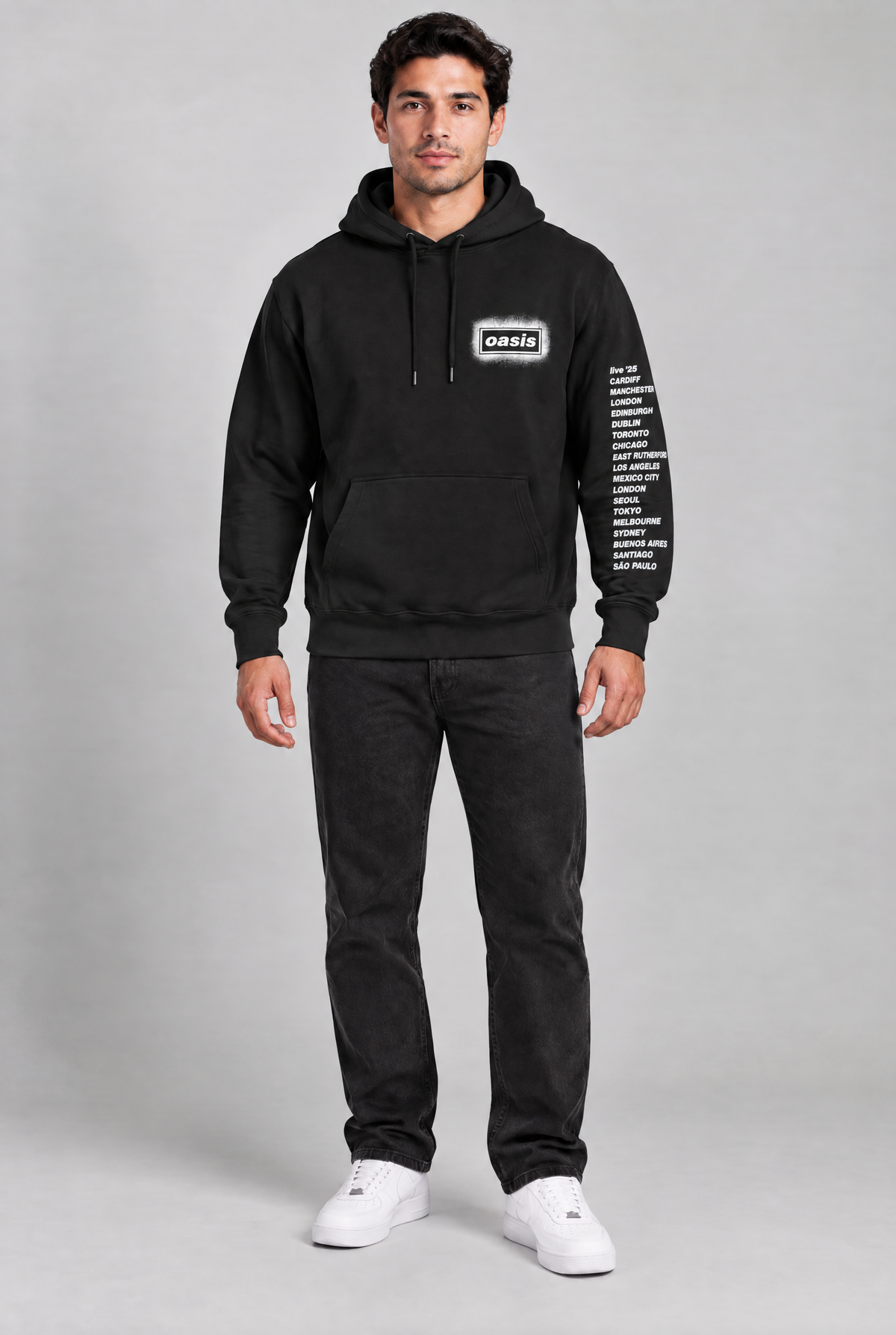 A man modeling a black pullover hoodie with a white 'Oasis' logo on the chest and white text printed down one sleeve,
